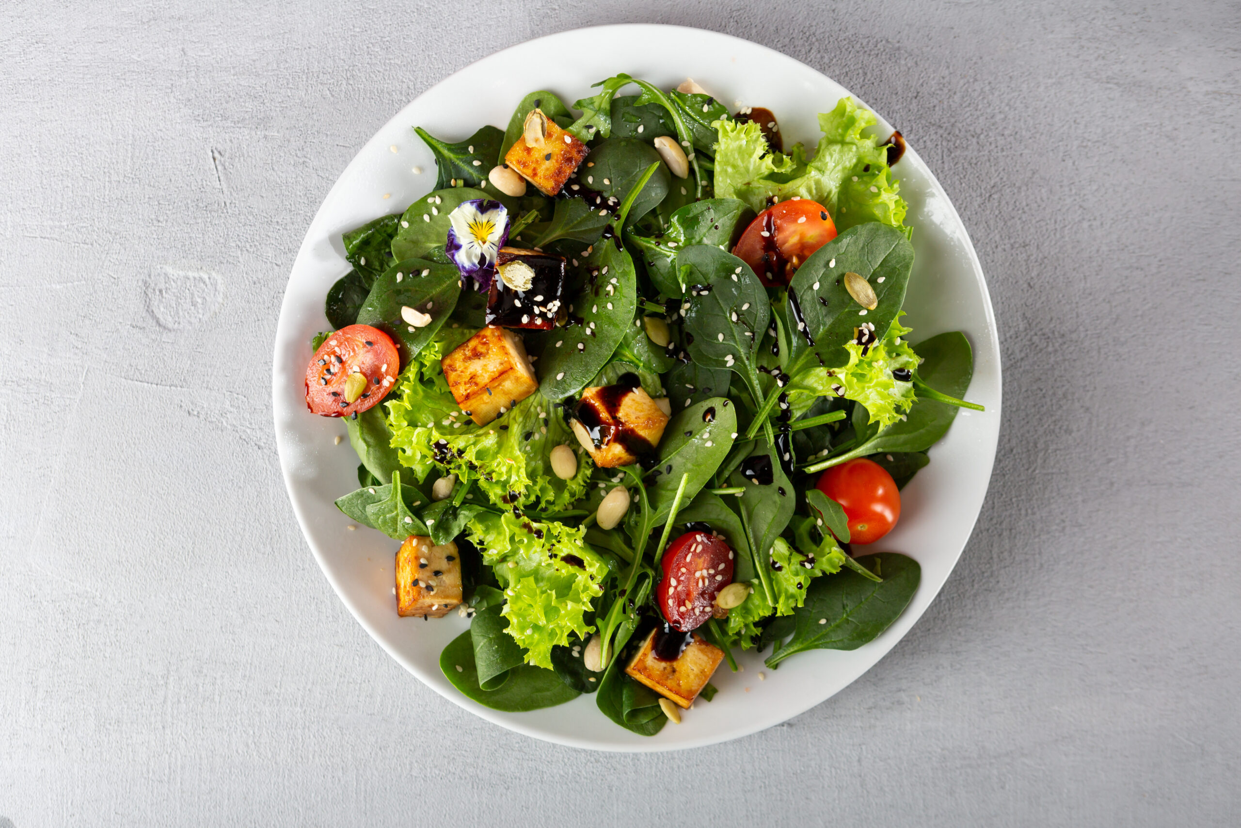 Overhead view of tofu salad and spinach on white plate